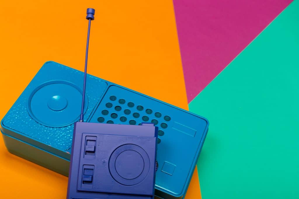 Altavoz portátil vintage en color azul sobre fondo de papel en tonos naranja, rosa y verde.