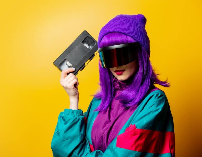 Estudio de Diseño Gráfico Creativo en Valencia y Yecla 47 Mujer con estilo retro futurista sosteniendo un cassette VHS, con chaqueta ochentera y peluca morada, concepto visual de nostalgia y estética vintage en marketing.