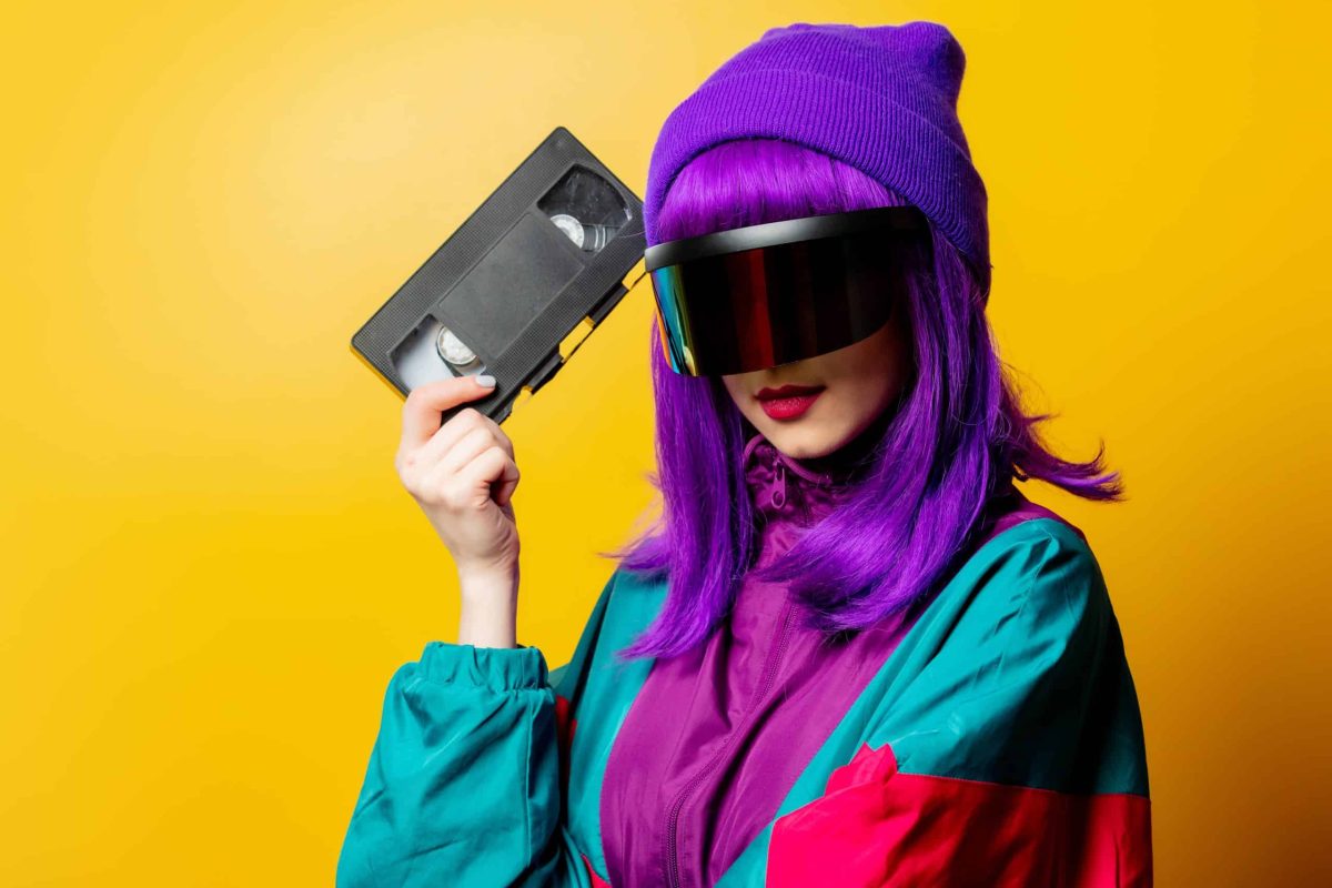 Mujer con estilo retro futurista sosteniendo un cassette VHS, con chaqueta ochentera y peluca morada, concepto visual de nostalgia y estética vintage en marketing.